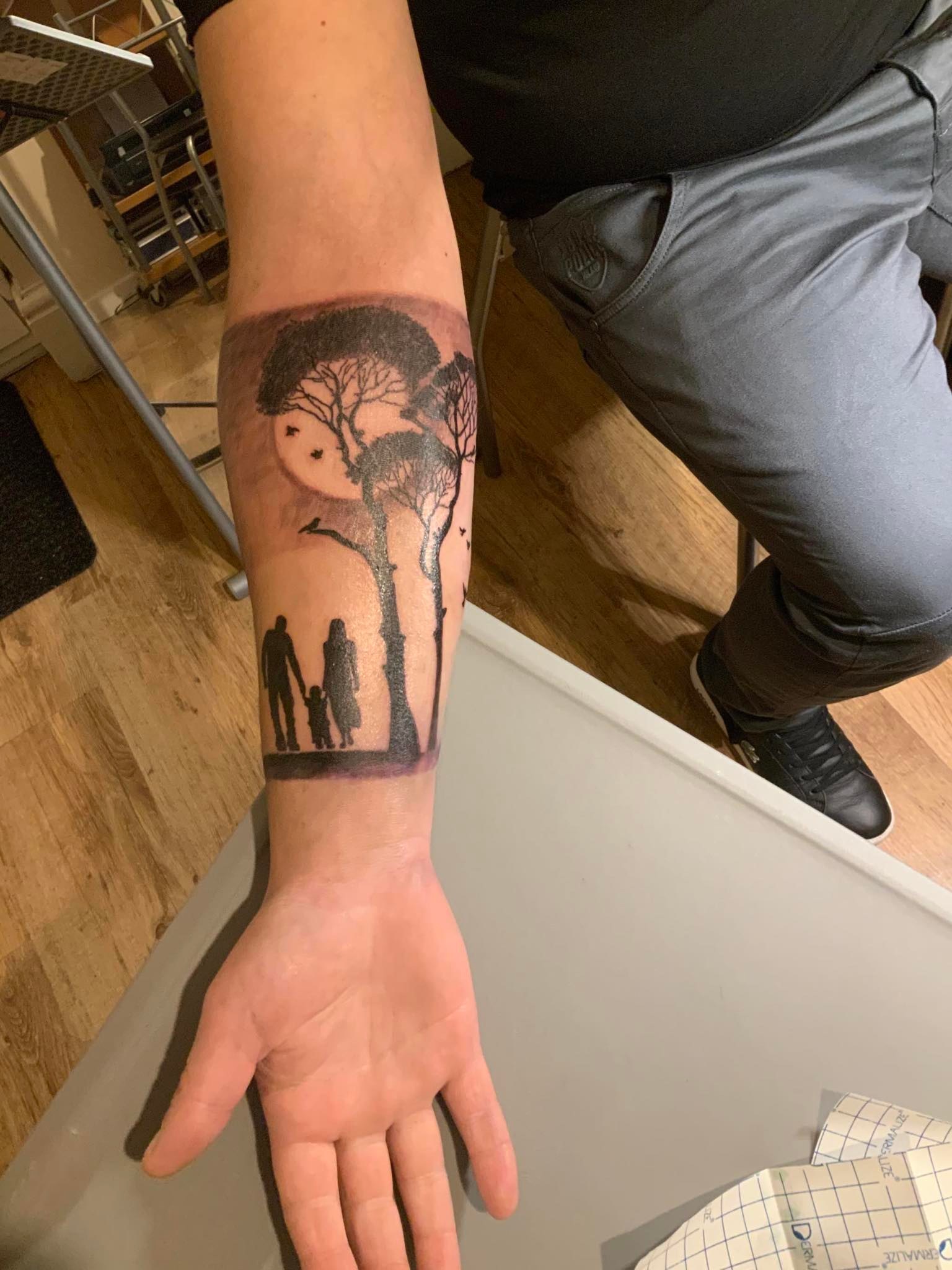 The forearm of a man that has a tattoo of a family in nature